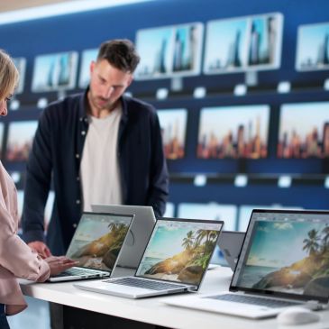 People browsing laptops in an electronics store with cityscape images on screens.