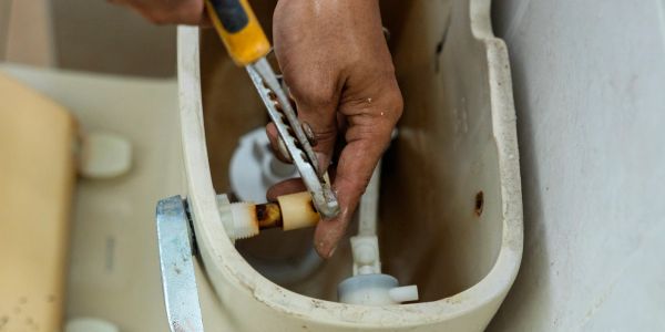 Person using pliers to fix a toilet tank component.
