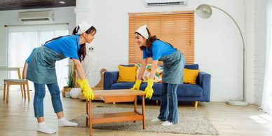 Two women cleaning and moving a coffee table.