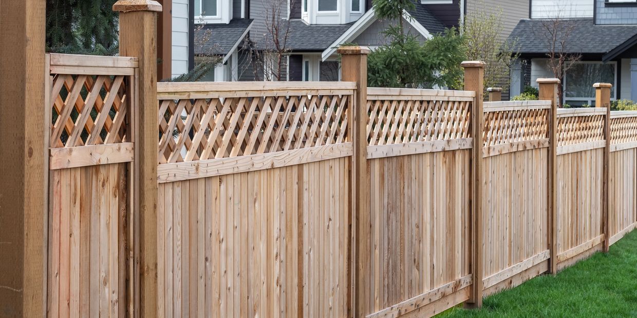 A wooden fence with lattice top panels in front of suburban houses.