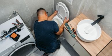 Person fixing a toilet in a bathroom.