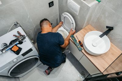 Man fixing a toilet in a bathroom.