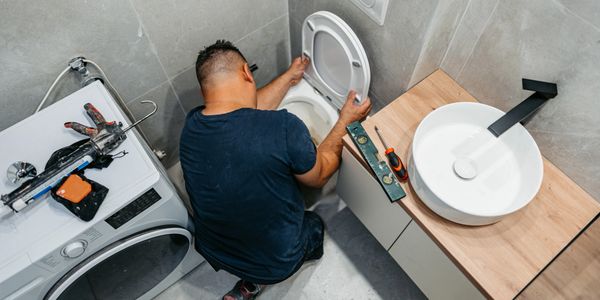 A man fixing a toilet seat in a modern bathroom.