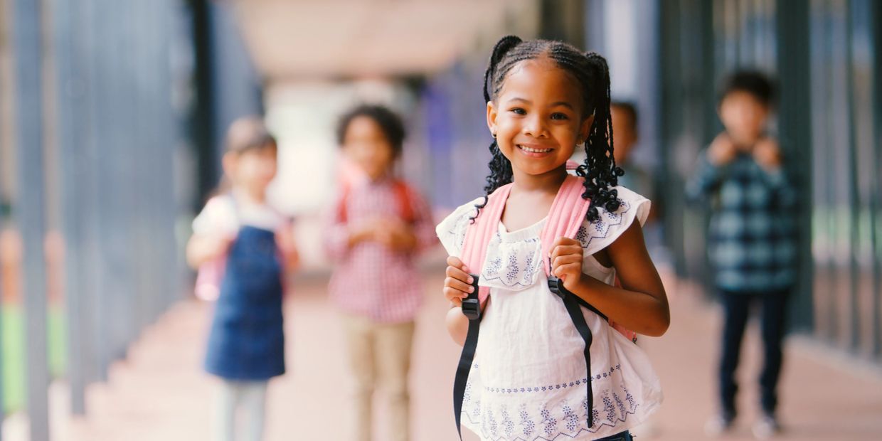 Smiling girl with backpack and children in background.