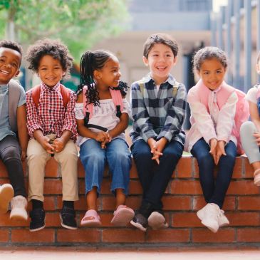 A group of six kids sitting on a brick wall, smiling and laughing.