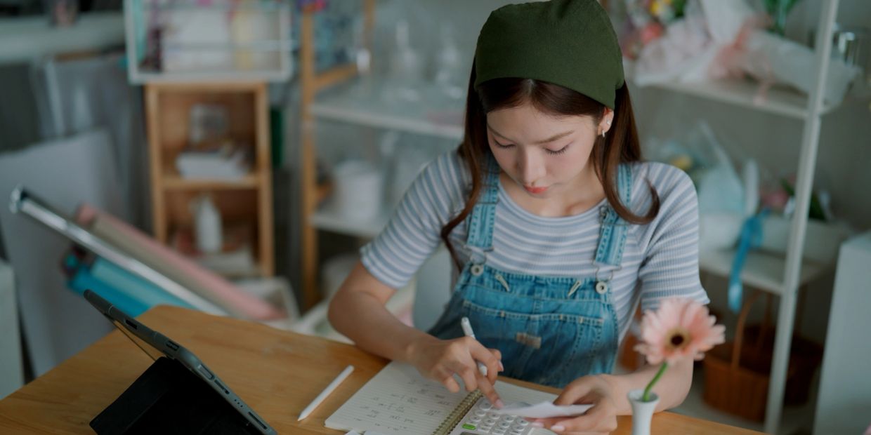 Young woman using calculator and tablet while working at a wooden table.