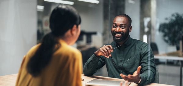 Two colleagues engaged in a friendly office conversation with smiles.