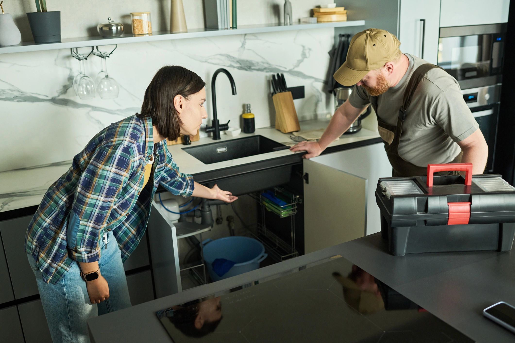 Homeowner showing a plumber a leak under her kitchen sink