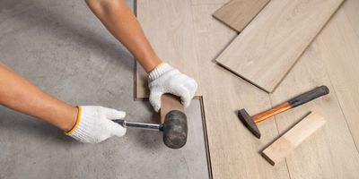 Person installing wooden flooring using a rubber mallet and gloves.