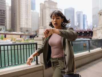 A woman looks at her watch while walking in a city.