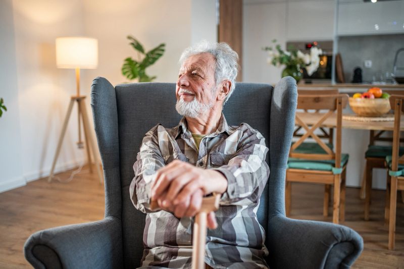 Happy elderly man resting in a comfortable armchair, enjoying his retirement in a cozy living room. Surrounded by warm decor and natural light, he embodies contentment and tranquility