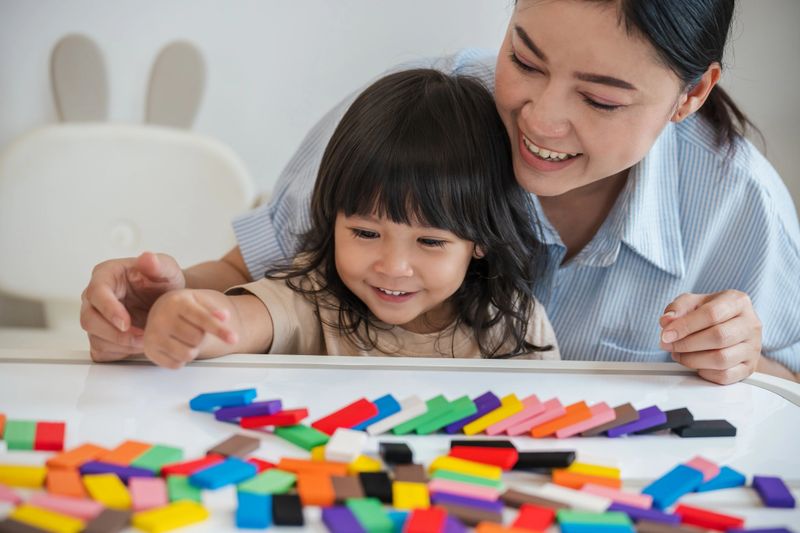 toddler girl and her mother playing colorful wooden block toy or domino game together