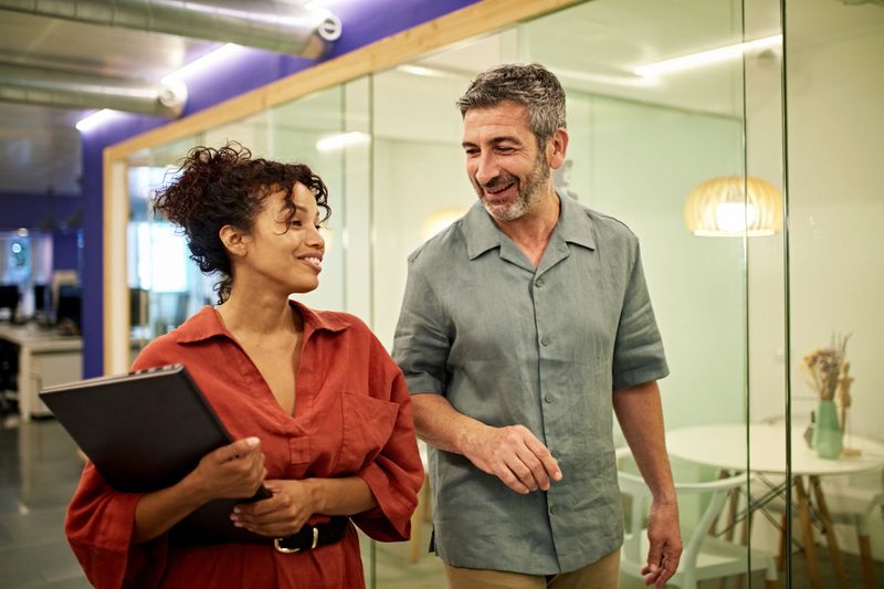 Male and female business professionals walking, talking, and smiling in modern office.