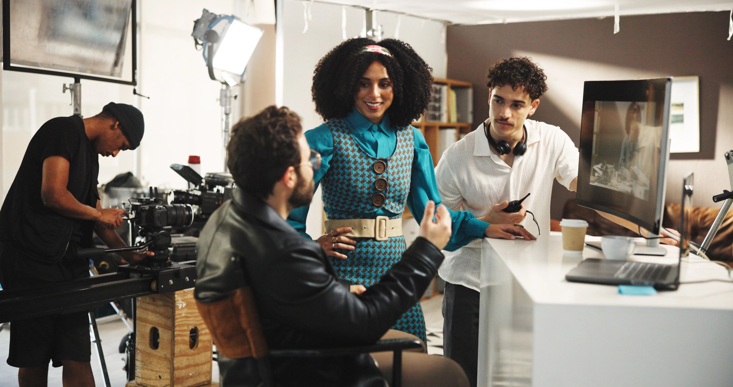 director talking to an actor and assistant director on set. A cameraman is setting up a camera