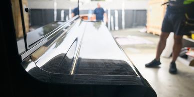 A glossy black piano being moved by two people outdoors. Commercial moving junk removal long distance moving packing services residential moving 