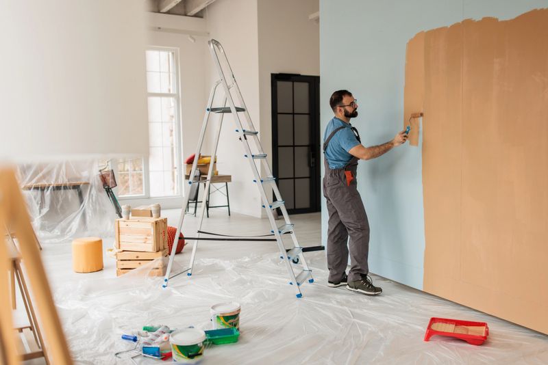 Focused man applying paint on wall surface, creating a brighter and modernized living area as part of home renovation.