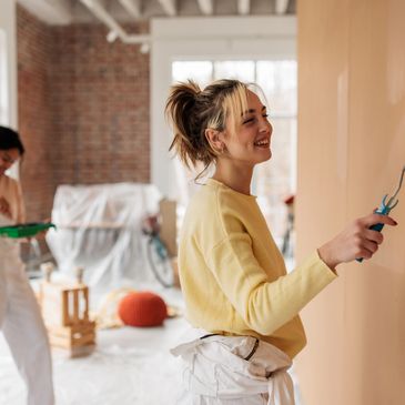 Two women painting a room with rollers, smiling and enjoying the activity.