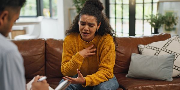 Black or biracial woman in therapy holding her chest with an anxious expression.