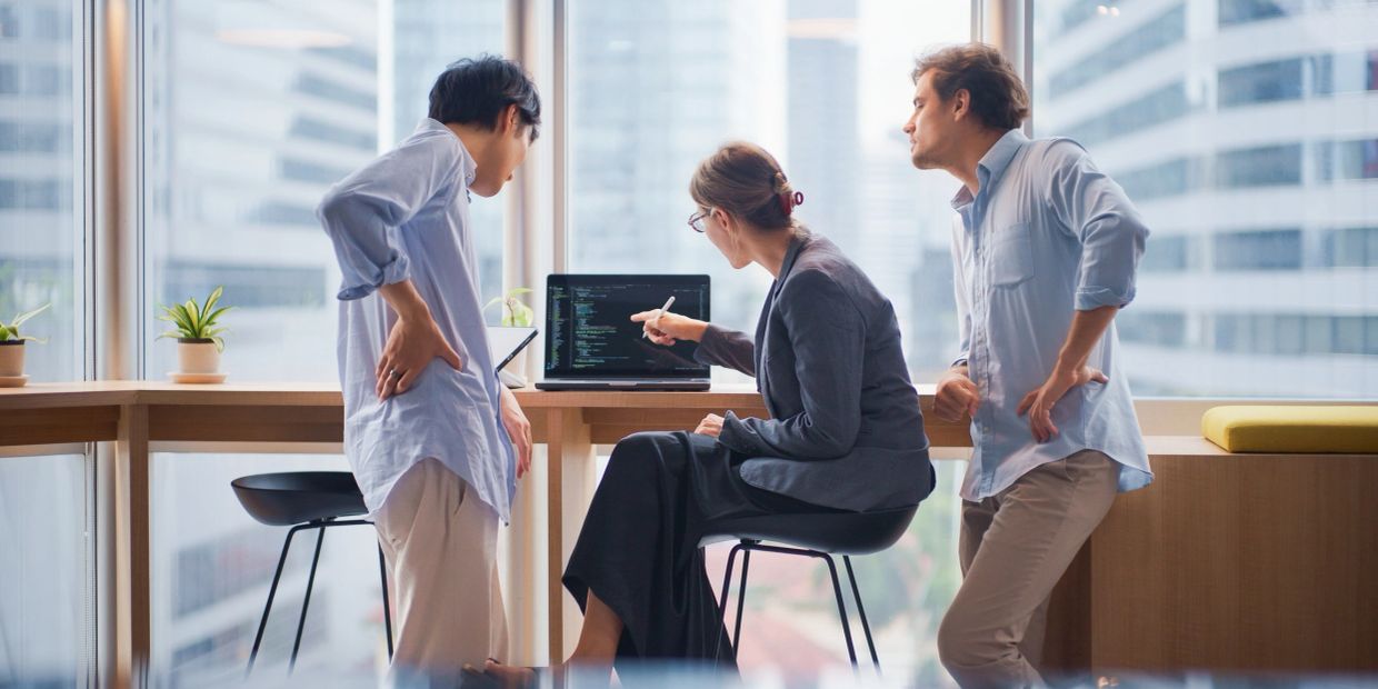 Three coworkers discuss code on a laptop in an office.