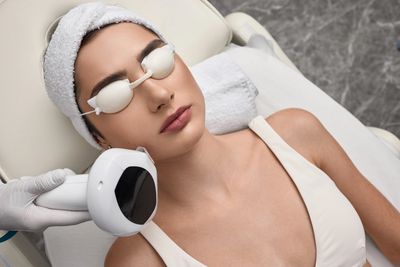 Woman receiving a facial laser treatment wearing protective goggles.