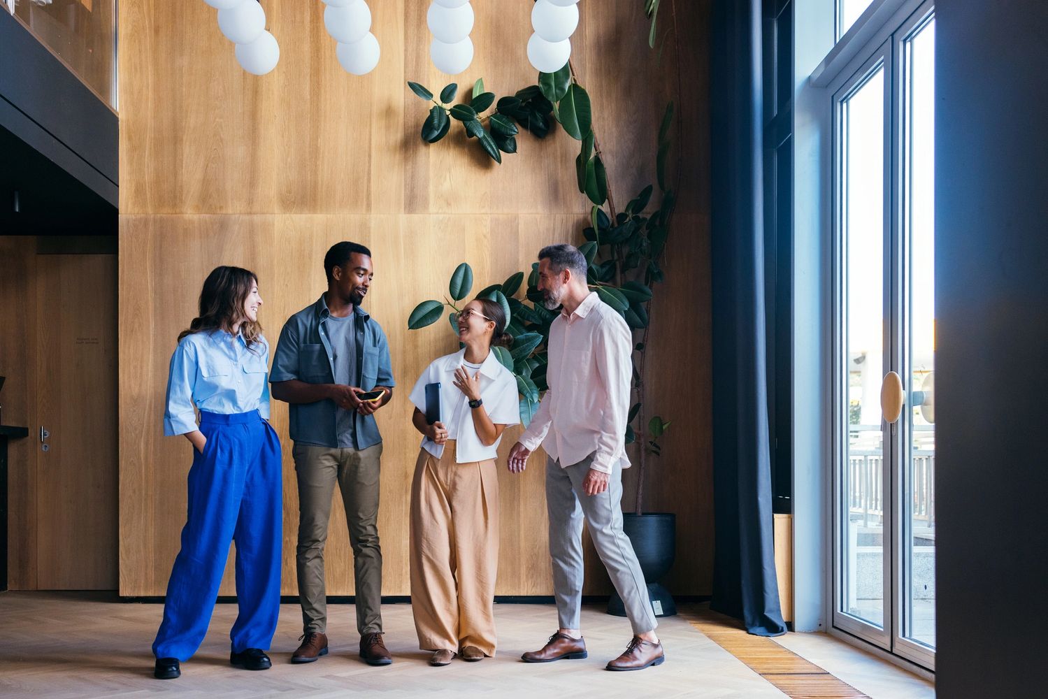 Four coworkers happily chatting in a modern office space with natural light and plants.
