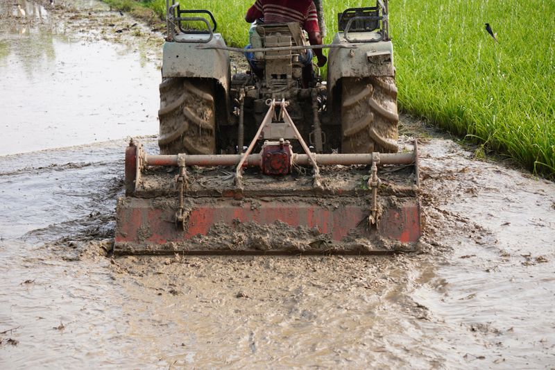 A rotary tiller being used in a muddy field, for preparing the soil for planting