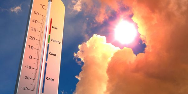 Thermometer showing hot temperature against a bright sunny sky.