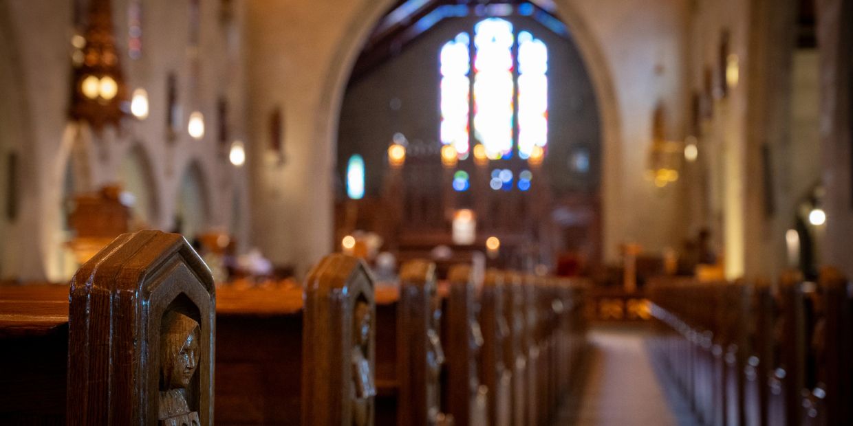 Wooden pews inside a church near stained glass windows.