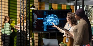 Two women discussing AI brain model on screen.