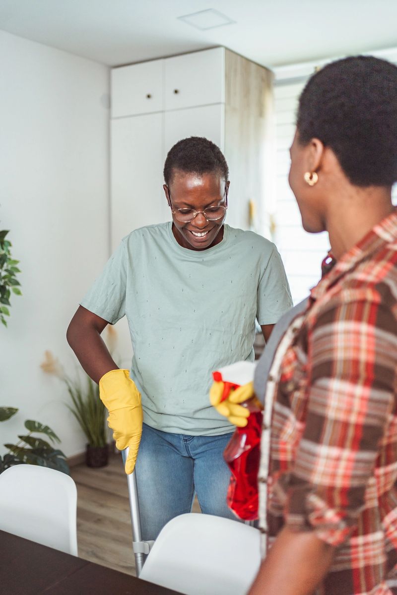 Two happy African American women are cleaning their home together, enjoying their time and smiling
