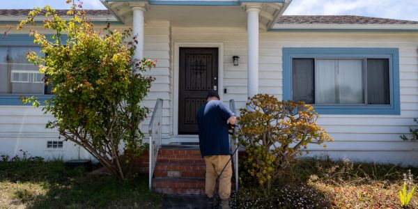 Man working on garden in front of a white house with blue trim.