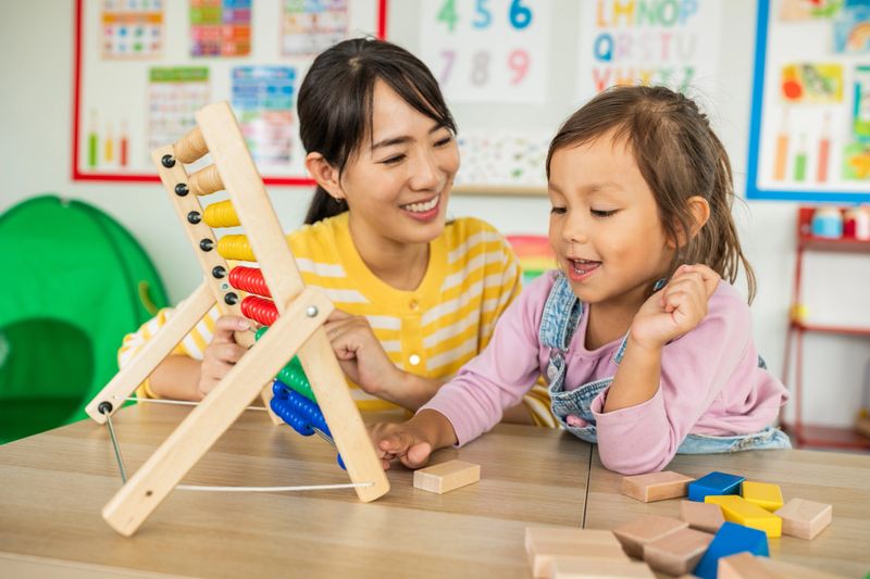 Preschool teacher with children playing with colorful wooden didactic toys at kindergarten.