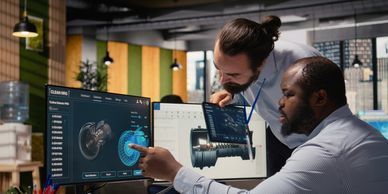 Two engineers analyze turbine designs on dual monitors in a modern office.