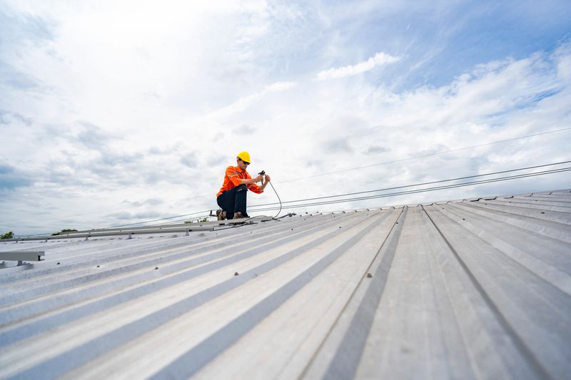 Technician in safety uniform and helmet kneeling on a rooftop, using a drill for precise installation work. A scene highlighting safety, professionalism, and technical expertise in construction.