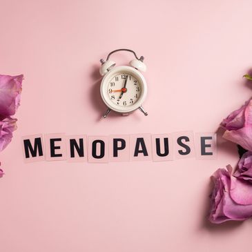 Clock and letters spelling menopause with roses on pink background.