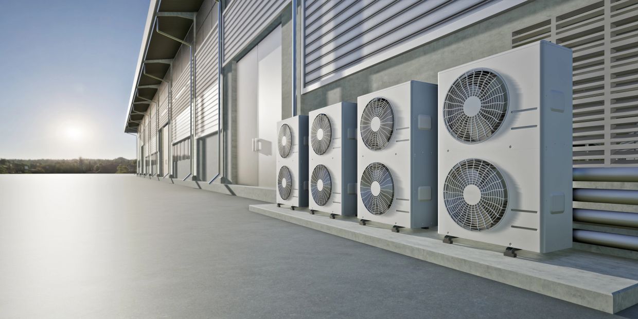 A row of outdoor air conditioning units against a large building.