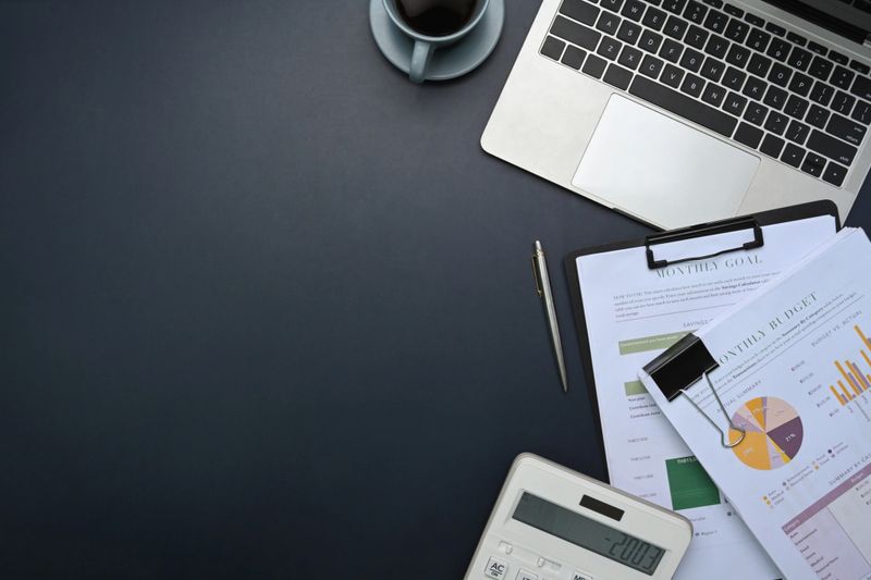 Top view of office desk with laptop, calculator, financial reports, and coffee cup on desk.