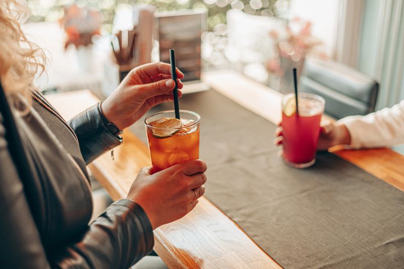Close-up of two people enjoying refreshing drinks with lime slices at a cozy cafe table, capturing a casual social moment of relaxation and conversation