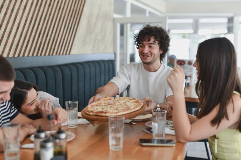 Diverse Group Of Friends Laughing And Sharing Moments While Eating Pizza At Restaurant