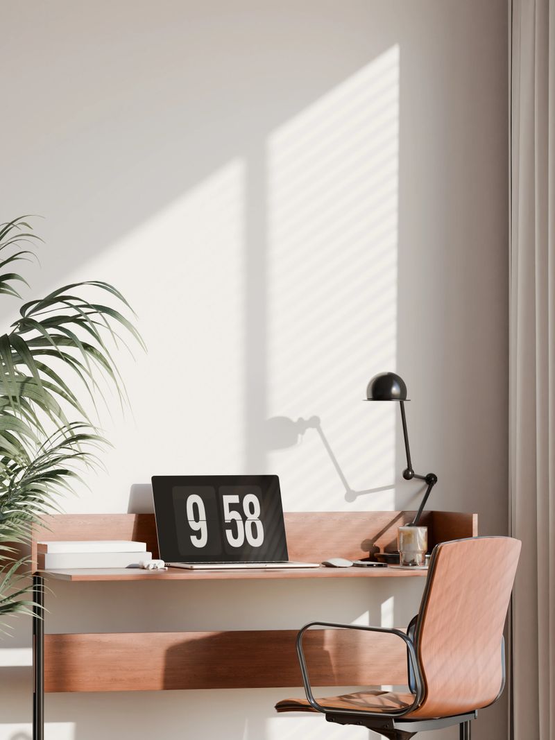 Modern home office interior with a minimalist design featuring a wooden desk, ergonomic chair, and a vertical blank frame mockup on the wall. Bright natural light, green plant decor, and an organized workspace setup make it ideal for showcasing poster designs, wall art, or home office inspiration.