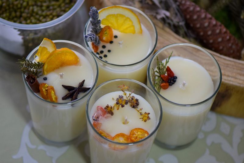 Candle making workshop scene with participants holding handmade soy candles decorated with dried fruits, herbs, and spices. Creative DIY activity, eco-friendly soy wax candles, and artisanal craft design.