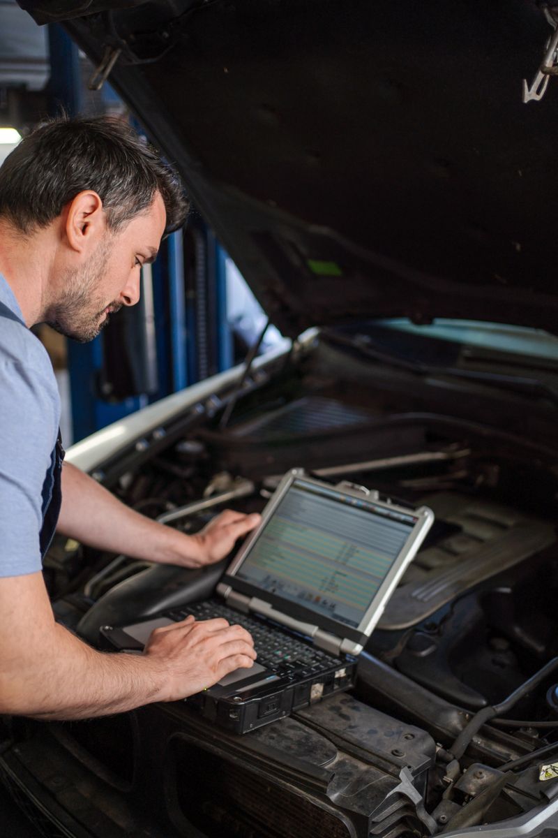 Car mechanic using diagnostic software on laptop, examining engine in auto repair shop