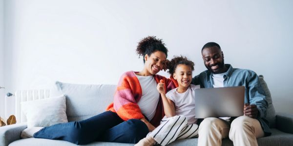 Family of three sitting on couch with laptop.