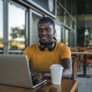Man using laptop at a cafe with headphones and coffee.