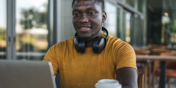 Man working on laptop with headphones around his neck.