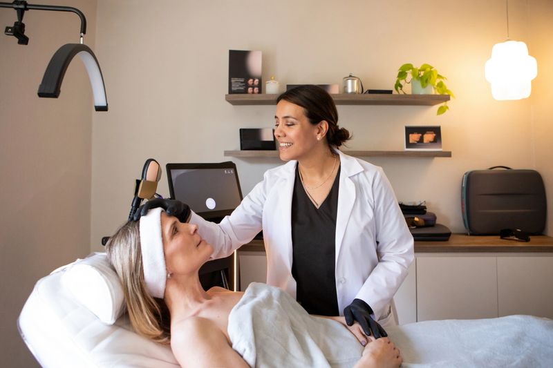 Beautiful Latin American dermatologist evaluating the skin and providing appropriate treatment for her female patient in the doctor's office - Buenos Aires, Argentina
