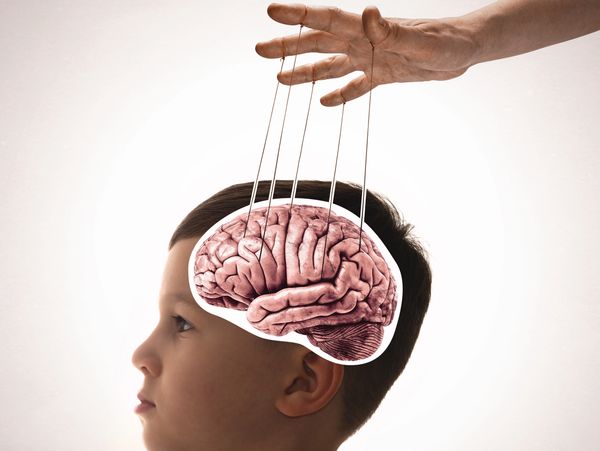 A hand manipulates a child's brain like a puppet with strings.