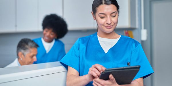 Healthcare workers in blue scrubs using digital devices in a clinical setting.