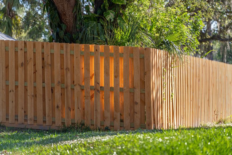 Wooden picket fence on green lawn surrounding property grounds for backyard protection and privacy.