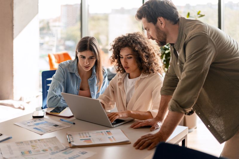 Three colleagues collaborating on a project, analyzing data on a laptop in a bright, modern office environment